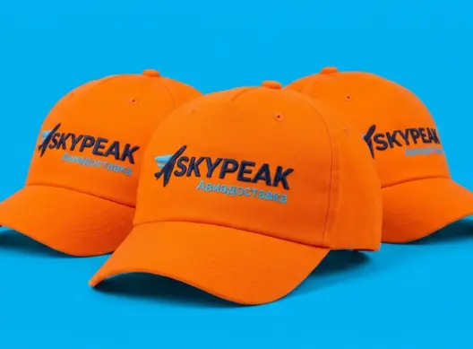 Три оранжевые бейсболки SkyPeak Logistics каскадом в ракурсе три четверти с вышивкой на передней панели