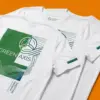 Три белые футболки с зелёным принтом GREEN AXIS, разложенные внахлёст на оранжевом фоне