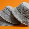 Три панамы из денима с acid wash в диагональной композиции, на переднем плане — металлическая пластина с гравировкой Nordic Peak
