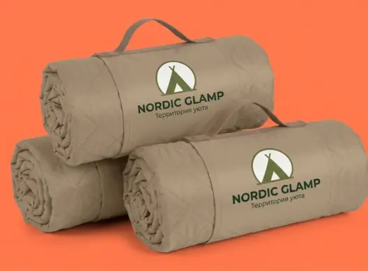 Три свернутых бежевых пледа Nordic Glamp сложены стопкой, логотип на переднем клапане