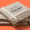 Стопка из трёх бежевых пледов Nordic Night с вышитым логотипом-горой на верхнем изделии
