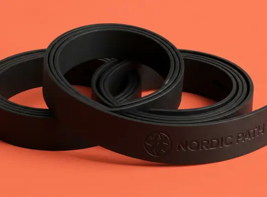 Три чёрных кожаных ремня Nordic Path, свёрнутых в кольца, на коралловом фоне — виден кончик с тиснением