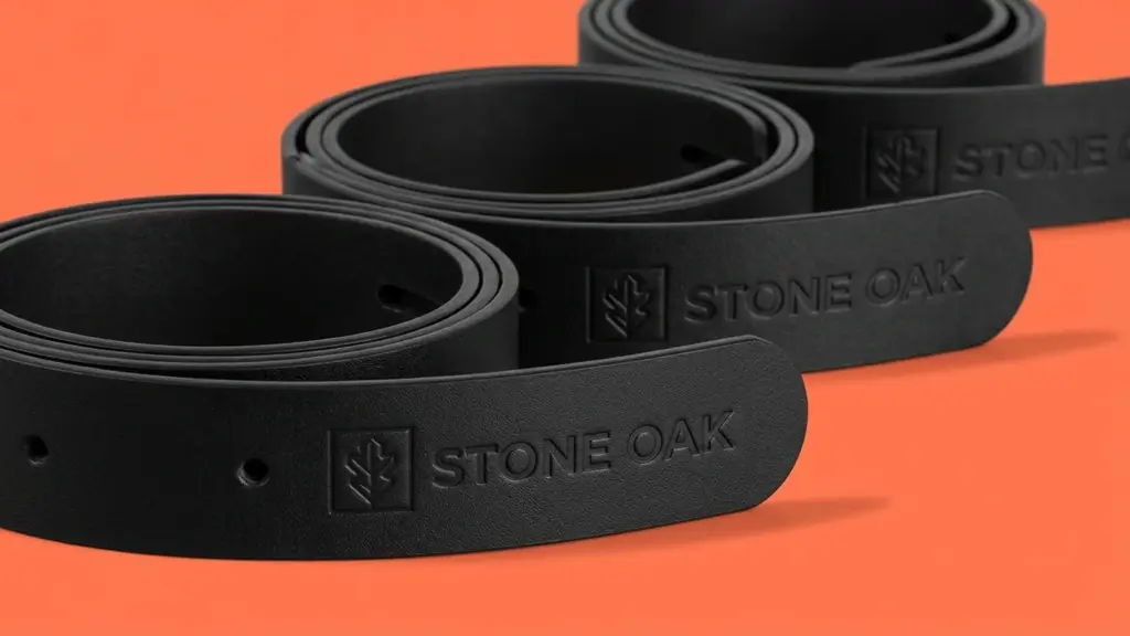 Три кожаных ремня Stone Oak свёрнуты спиралью и выстроены под углом, тиснение логотипа на кончике переднего изделия