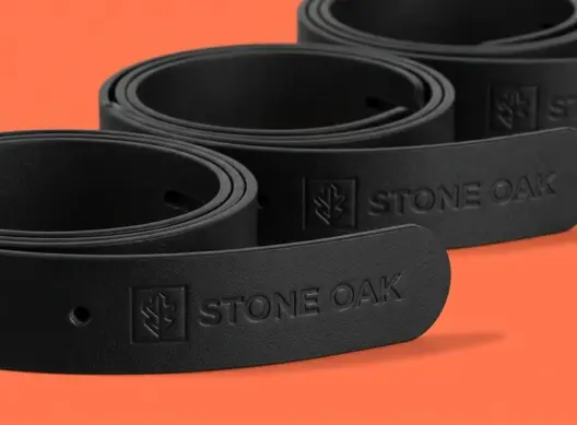 Три кожаных ремня Stone Oak свёрнуты спиралью и выстроены под углом, тиснение логотипа на кончике переднего изделия