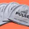Три шапки-бини PULSE веером на коралловом фоне — видны объём и логотип на передней