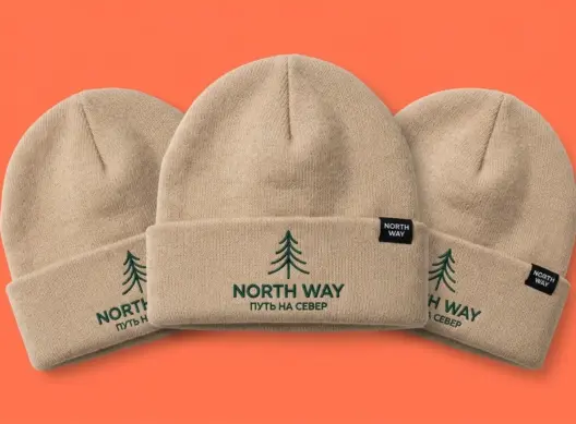 Три бежевые шапки-бини NORTH WAY веером на коралловом фоне — видны купол и вышивка на отвороте
