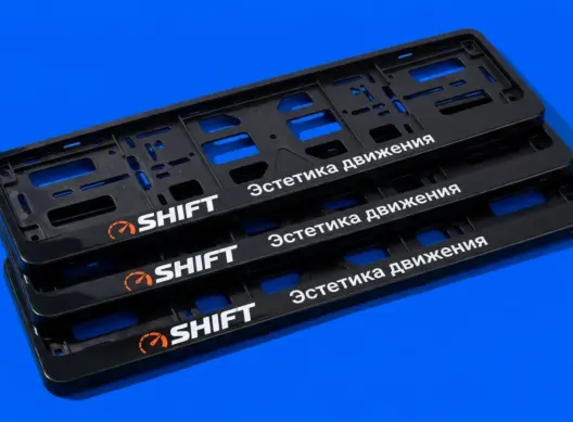 Три глянцевые рамки для номера SHIFT уложены каскадом под углом, оранжевый логотип контрастирует с чёрным пластиком