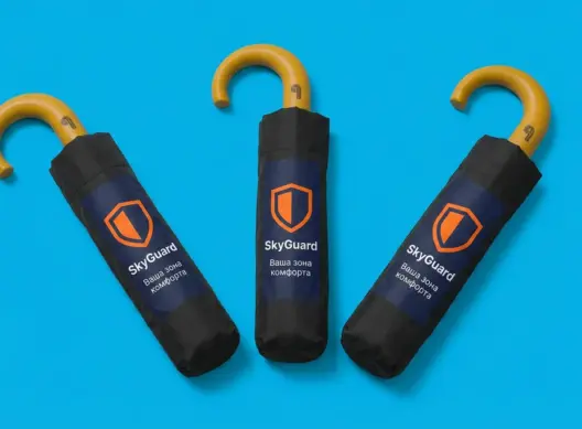 Три складных зонта SkyGuard в чёрных чехлах веером на голубом фоне с логотипом и слоганом бренда