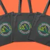 Три тёмно-серые сумки-шопера ECO-SQUAD с логотипом в кислотно-зелёных цветах, расположены внахлёст под углом три четверти